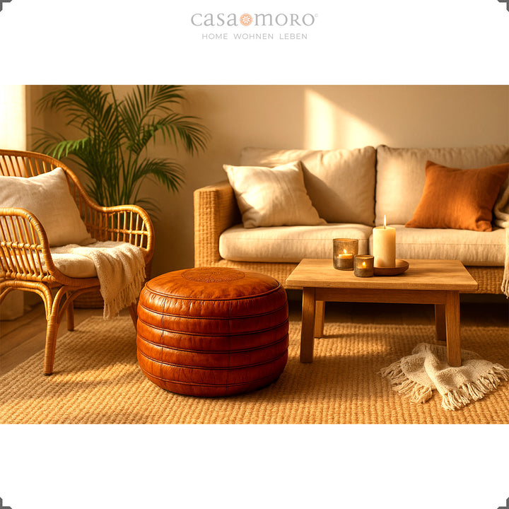 Wohnszene im Boho-Stil mit rundem Leder Pouf in warmem Braun vor Sofa und Rattansessel, umgeben von Kerzenlicht und Naturmaterialien – harmonisches Ambiente.