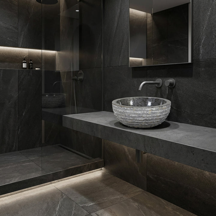 Rundes Aufsatzbecken aus Stein auf schwebender Konsole, modernes Bad mit dunklen Fliesen, Glasdusche und indirektem Licht