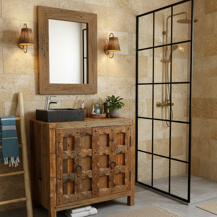 Eckiges Waschbecken aus Stein mit dunkler Oberfläche auf rustikalem Holzwaschtisch im warmen Badezimmer, kombiniert mit verchromter Armatur, Holzspiegel und schwarzer Duschabtrennung