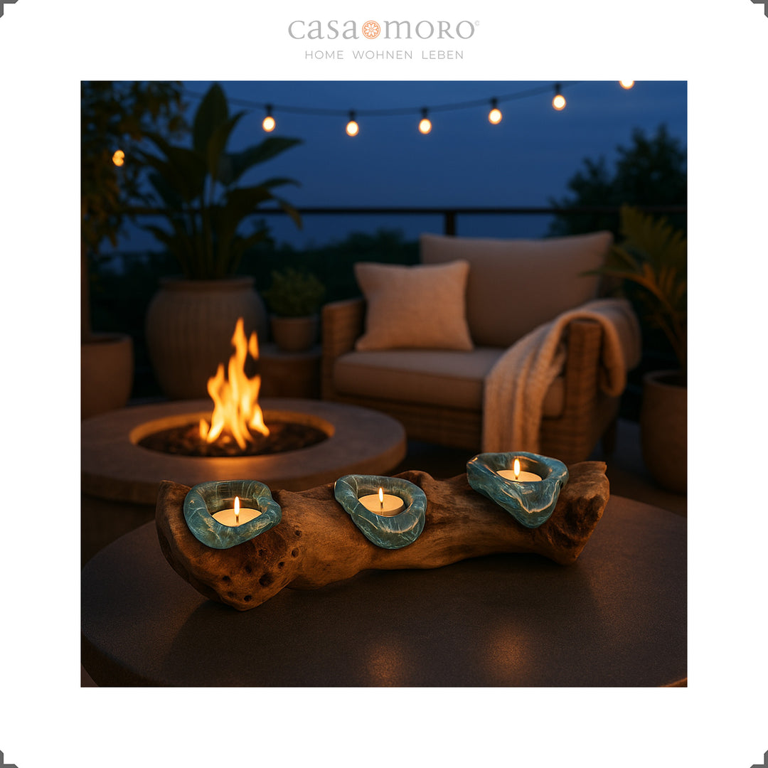 Teelichthalter aus Glas und Wurzelholz auf einer Terrasse bei Dämmerung, umgeben von Feuerstelle und Boho-Outdoordekor