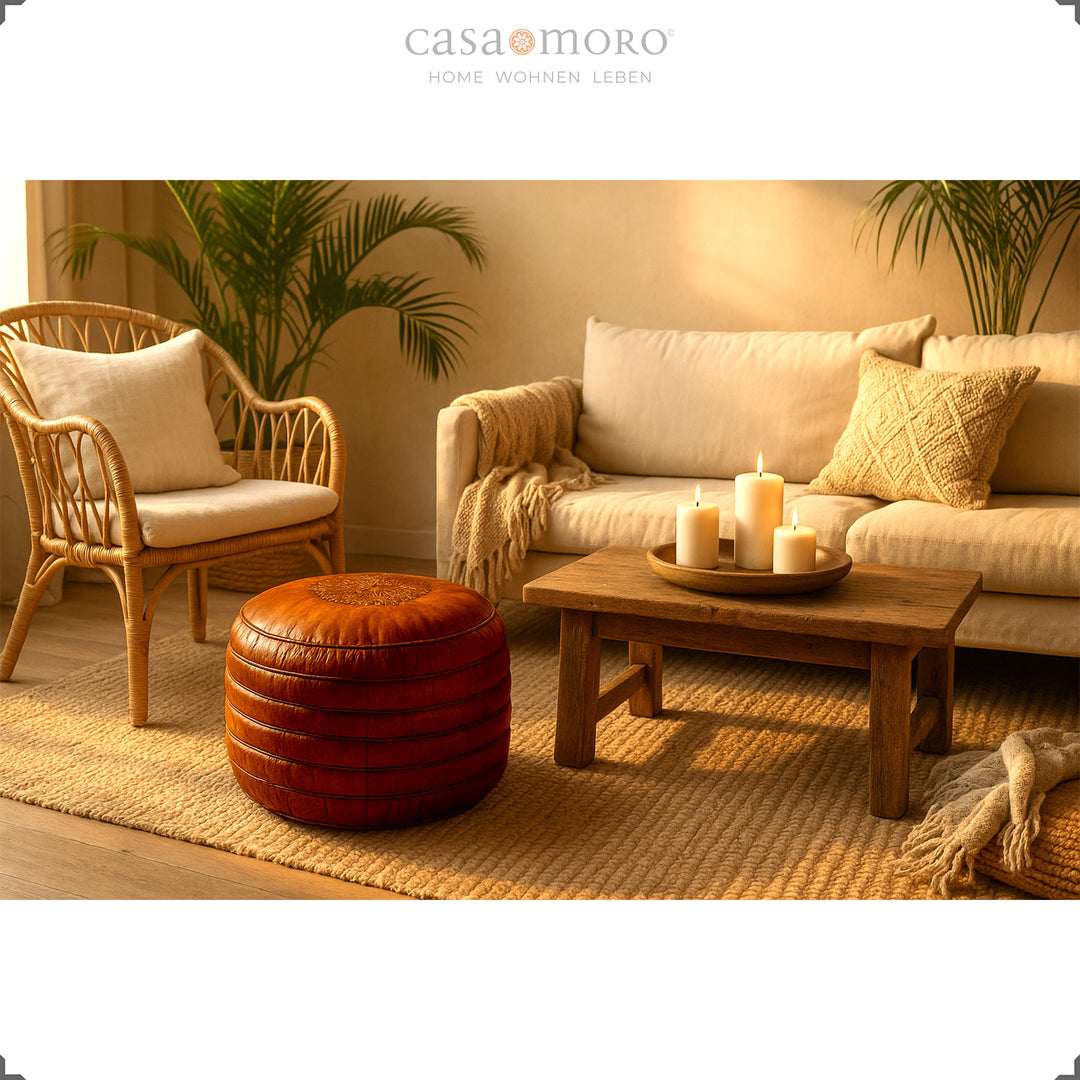 Warme Wohnzimmer-Szene mit rundem Echtleder Pouf in Braun vor Sofa und Holztisch mit Kerzen – gemütliche Boho-Atmosphäre im Abendlicht.