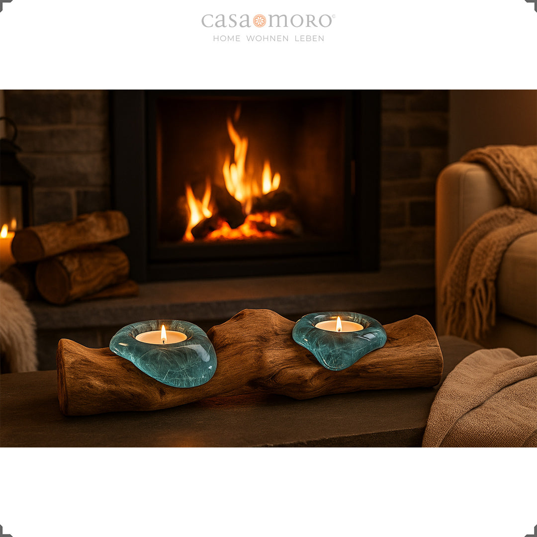 Teelichthalter aus Glas und Wurzelholz vor einem Kamin, sein sanftes Licht verstärkt die gemütliche Wohnstimmung.