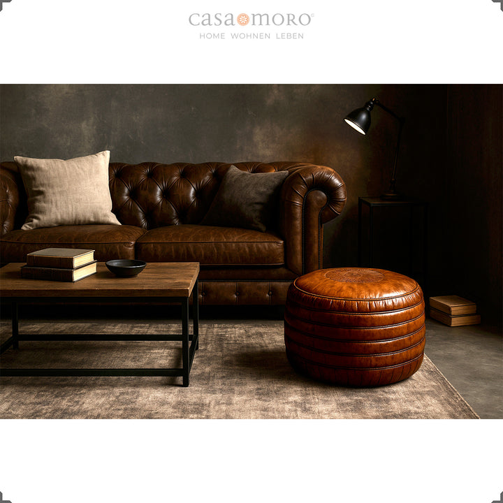 Elegantes Wohnzimmer mit Chesterfield-Sofa, Couchtisch und rundem Leder Pouf in Braun – stilvolle Szene im Industrial- und Modern-Rustic-Stil.
