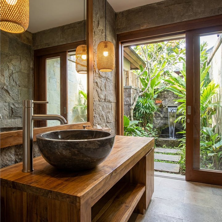 Rundes Aufsatzbecken aus dunklem Marmor auf Holzwaschtisch mit Edelstahlarmatur im offenen Spa-Bad mit Gartenblick
